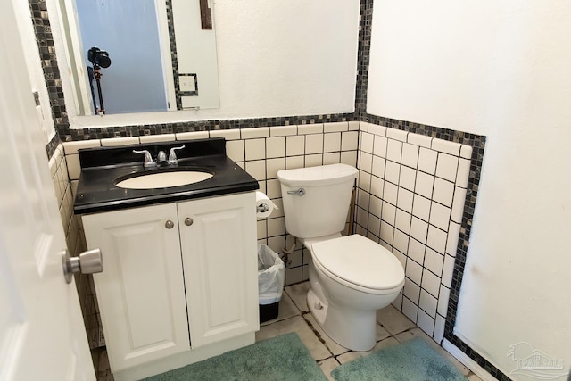 half bath with tile walls, toilet, wainscoting, tile patterned flooring, and vanity