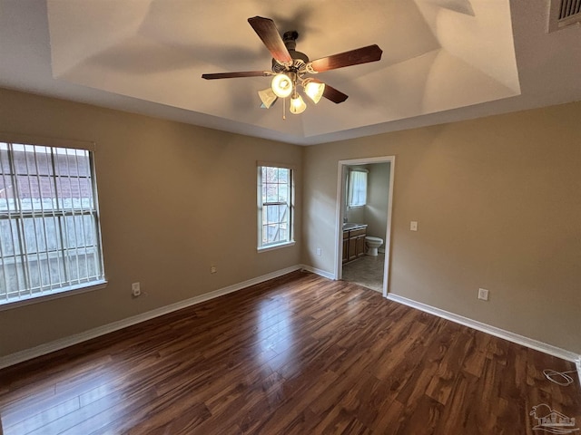 unfurnished bedroom with ceiling fan, dark hardwood / wood-style floors, connected bathroom, and a tray ceiling