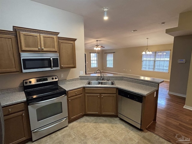 kitchen with kitchen peninsula, appliances with stainless steel finishes, ceiling fan with notable chandelier, sink, and light hardwood / wood-style floors