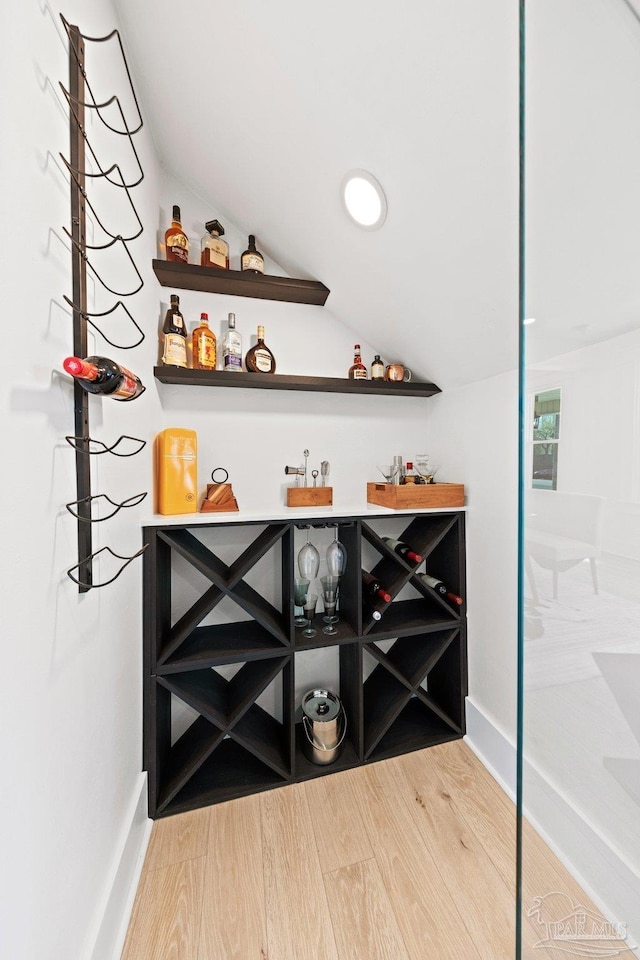 bar featuring a dry bar, baseboards, lofted ceiling, and wood finished floors