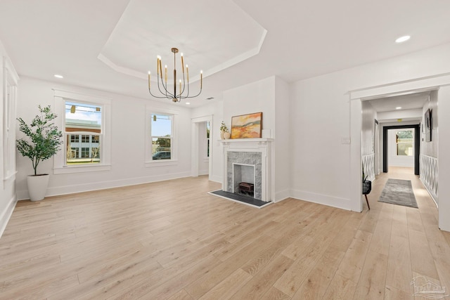 unfurnished living room featuring a tray ceiling, plenty of natural light, a fireplace, and light wood finished floors