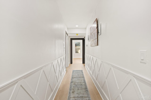 hallway with a decorative wall, light wood-style flooring, and a wainscoted wall