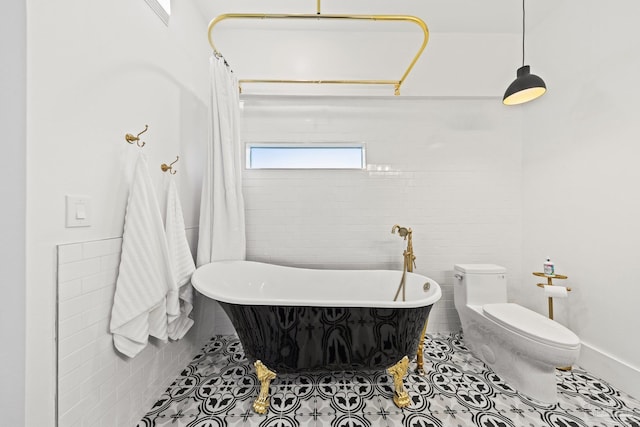 bathroom with tile patterned floors, toilet, tile walls, and a freestanding bath