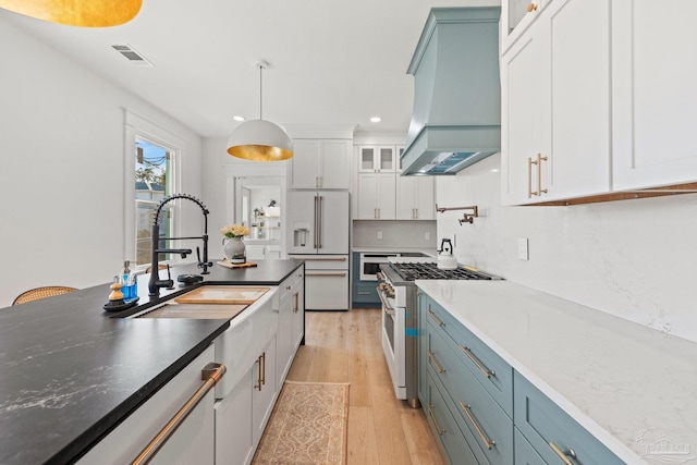 kitchen featuring visible vents, premium range hood, light wood finished floors, a sink, and high quality appliances