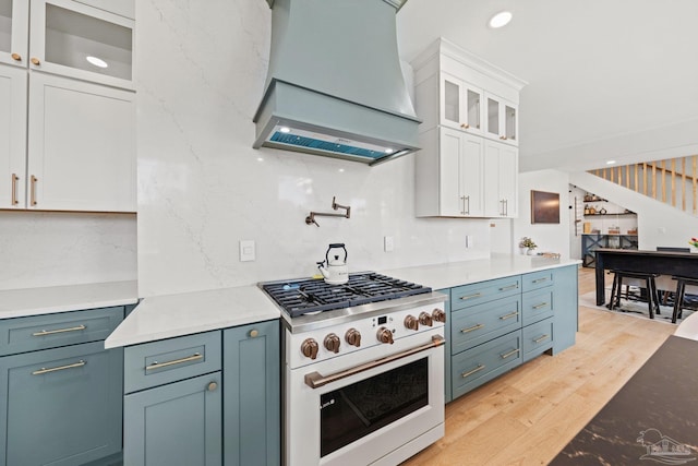 kitchen featuring high end white range oven, custom exhaust hood, white cabinets, light wood-style floors, and glass insert cabinets