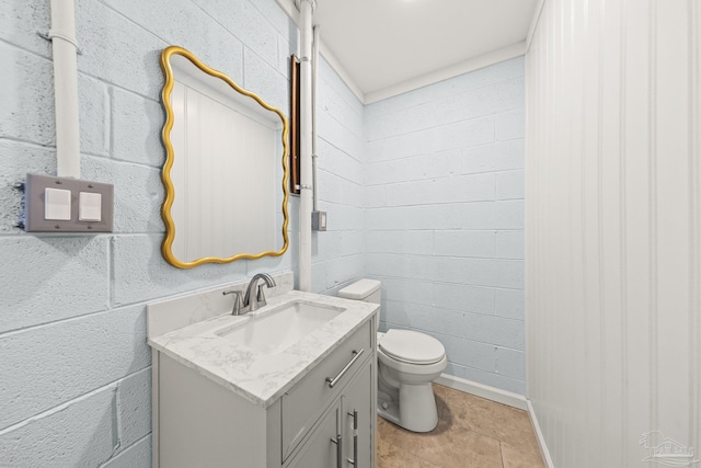 half bathroom featuring vanity, concrete block wall, and toilet