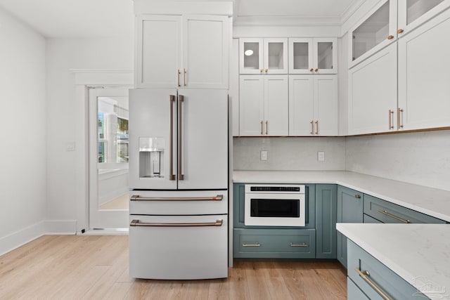 kitchen featuring glass insert cabinets, light countertops, light wood-style floors, white cabinets, and white appliances