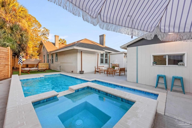 view of swimming pool featuring fence, a pool with connected hot tub, and a patio area