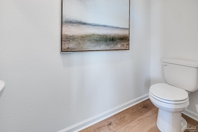 bathroom featuring baseboards, wood finished floors, and toilet