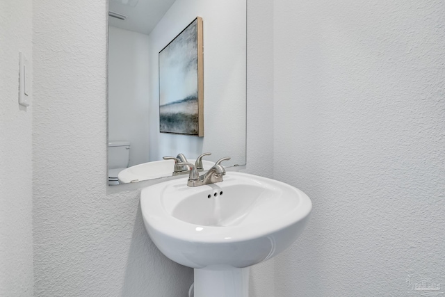 half bath with a textured wall and a sink
