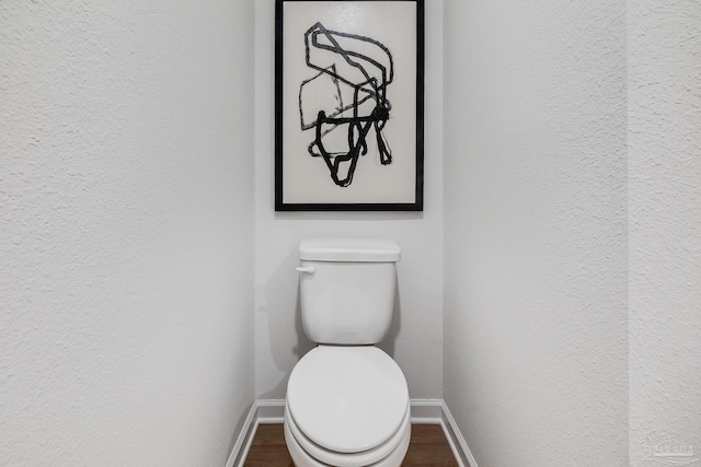 bathroom featuring baseboards, wood finished floors, a textured wall, and toilet