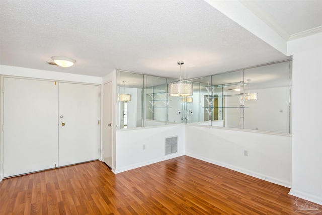 unfurnished dining area featuring a textured ceiling, wood finished floors, visible vents, and baseboards