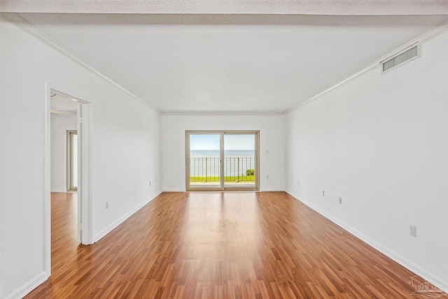 spare room with ornamental molding, wood finished floors, visible vents, and baseboards