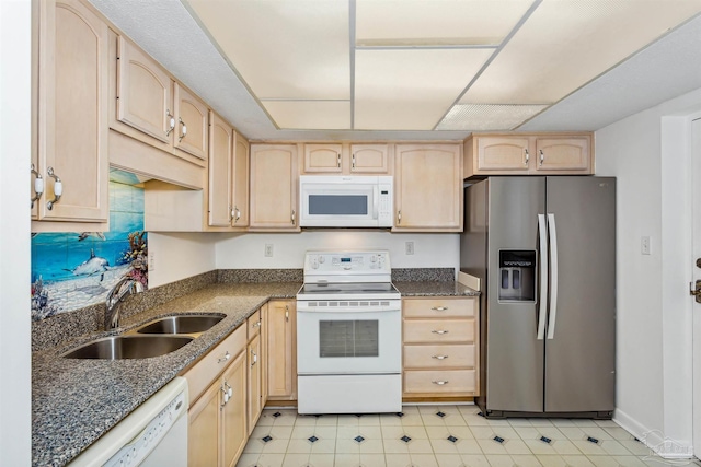 kitchen with dark stone countertops, white appliances, sink, and light brown cabinetry