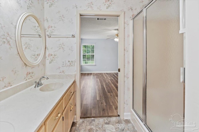 bathroom with ceiling fan, hardwood / wood-style floors, an enclosed shower, a textured ceiling, and vanity