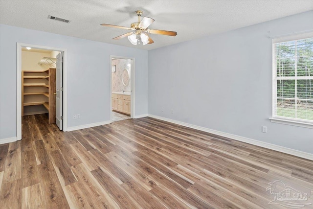 unfurnished bedroom with ceiling fan, wood-type flooring, a spacious closet, and multiple windows