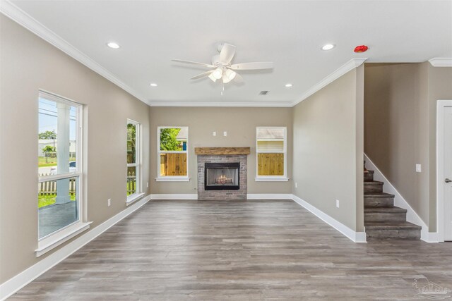 unfurnished living room featuring a stone fireplace, ceiling fan, wood-type flooring, and ornamental molding