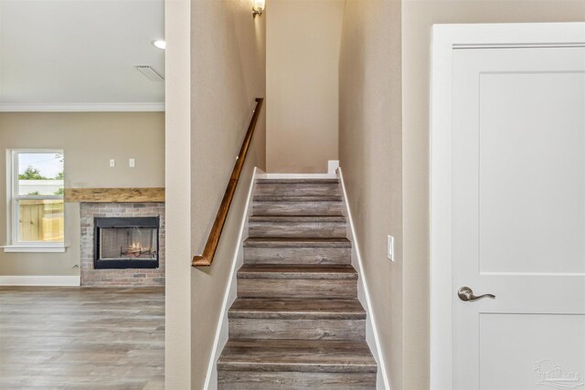 staircase with wood-type flooring, a brick fireplace, and crown molding