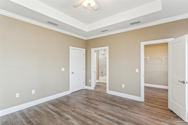 unfurnished bedroom featuring a tray ceiling, ceiling fan, ensuite bathroom, wood-type flooring, and a closet