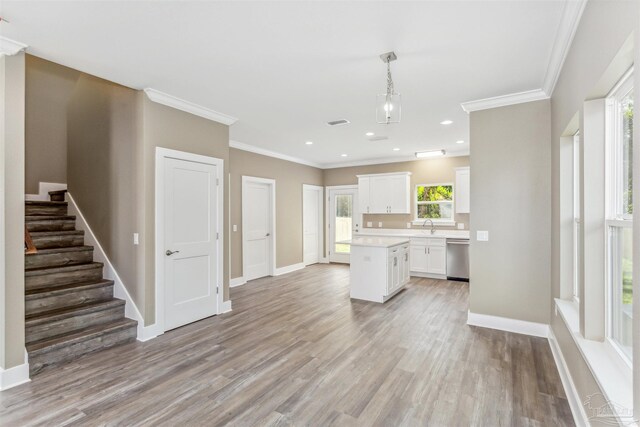 kitchen featuring light wood-type flooring, white cabinets, a kitchen island, stainless steel dishwasher, and pendant lighting