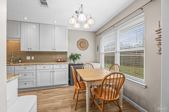 dining space featuring a notable chandelier, sink, a textured ceiling, and light wood-type flooring