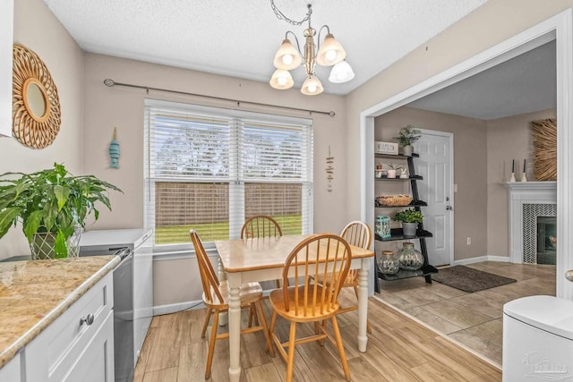 dining room featuring a textured ceiling, a notable chandelier, a fireplace, and light hardwood / wood-style flooring