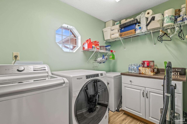 clothes washing area with a textured ceiling, cabinets, washing machine and clothes dryer, and light wood-type flooring