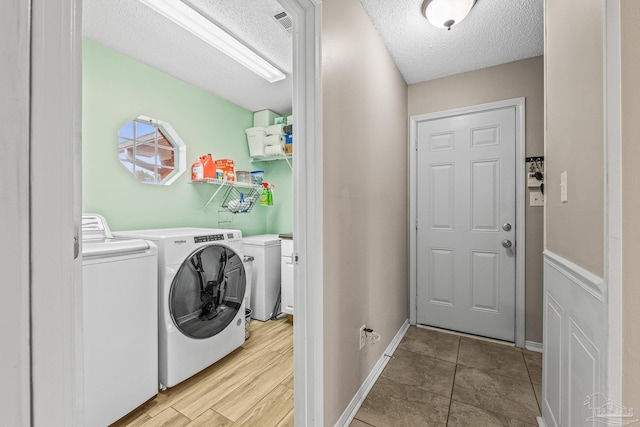 laundry area with light wood-type flooring, washing machine and clothes dryer, and a textured ceiling