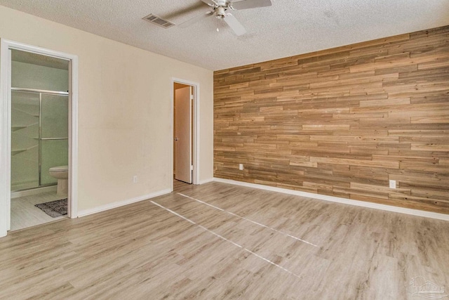 spare room with ceiling fan, light wood-type flooring, a textured ceiling, and wooden walls