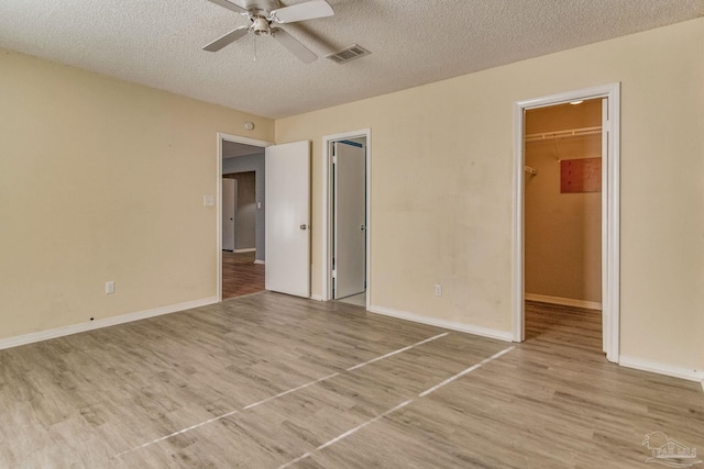 unfurnished bedroom with ceiling fan, a closet, a walk in closet, and light hardwood / wood-style flooring