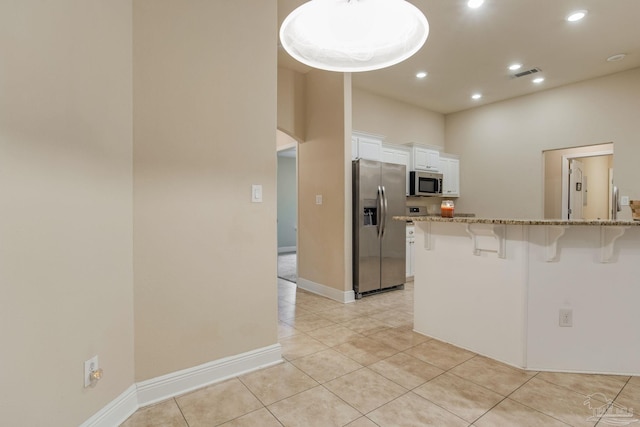 kitchen featuring white cabinetry, a kitchen breakfast bar, appliances with stainless steel finishes, light tile patterned floors, and light stone countertops