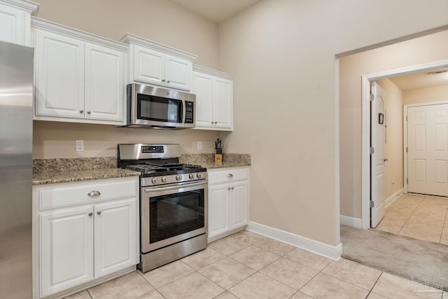 kitchen with appliances with stainless steel finishes, white cabinetry, light tile patterned floors, and light stone counters