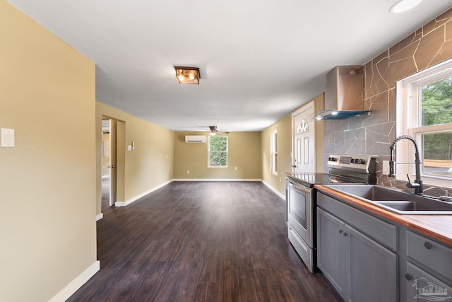 kitchen featuring gray cabinetry, wall chimney range hood, electric range, and plenty of natural light