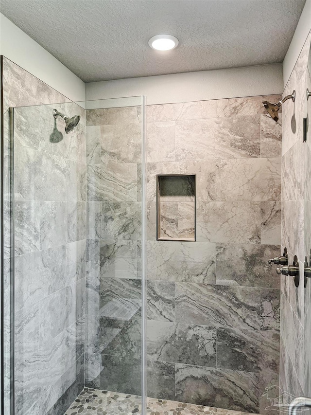 bathroom with a textured ceiling and tiled shower