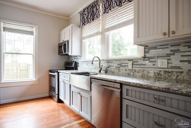 kitchen featuring tasteful backsplash, ornamental molding, light stone counters, stainless steel appliances, and light wood-type flooring