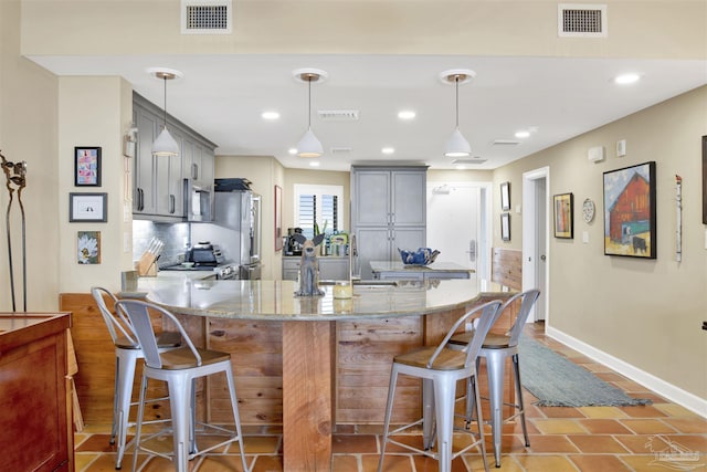 kitchen featuring gray cabinetry, sink, a kitchen breakfast bar, pendant lighting, and appliances with stainless steel finishes