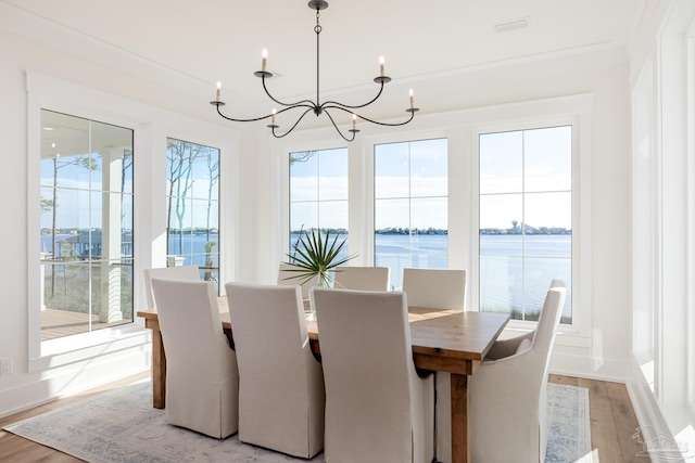 dining space with light hardwood / wood-style flooring, a water view, an inviting chandelier, and ornamental molding