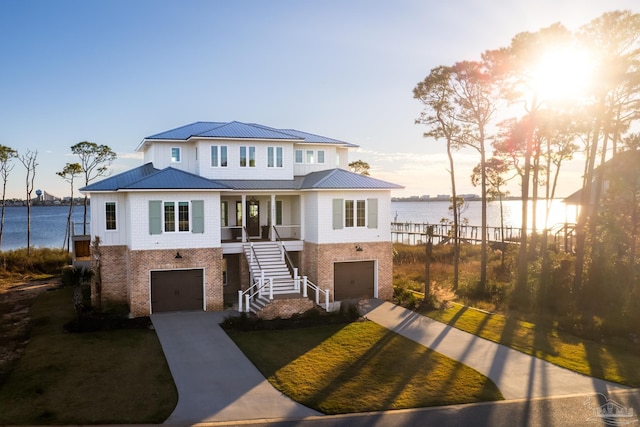 view of front of house with covered porch, a garage, a water view, and a lawn