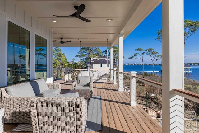 wooden deck with outdoor lounge area, ceiling fan, and a water view