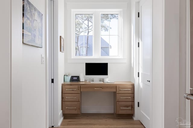 home office with built in desk and light hardwood / wood-style flooring