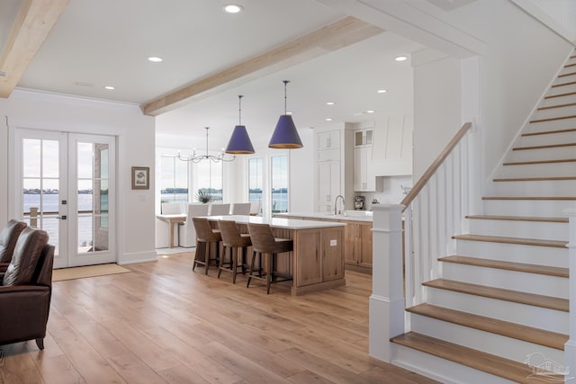 kitchen with beam ceiling, white cabinetry, sink, light hardwood / wood-style flooring, and a spacious island