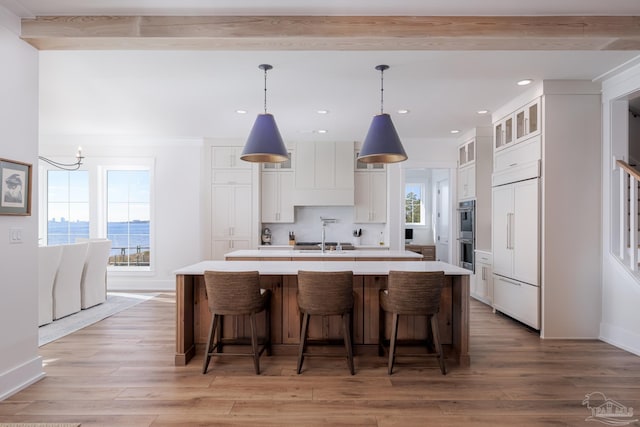 kitchen featuring white cabinets, an island with sink, a water view, and pendant lighting