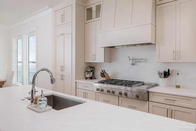 kitchen with white cabinets, sink, ornamental molding, custom range hood, and stainless steel gas cooktop