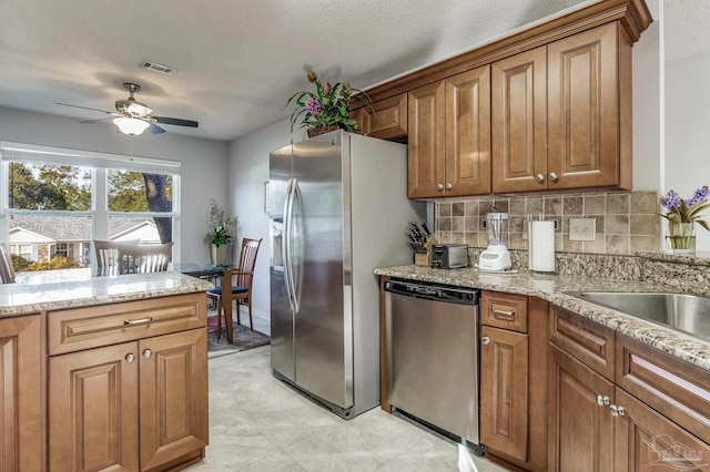 kitchen with ceiling fan, light stone counters, backsplash, a textured ceiling, and appliances with stainless steel finishes