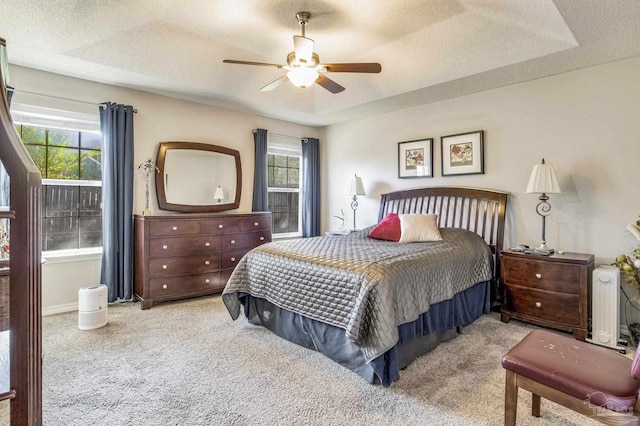 bedroom with a tray ceiling, ceiling fan, light carpet, and a textured ceiling