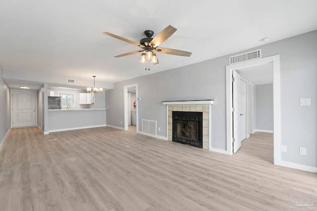 14100 River Rd Unit 223B, Pensacola, FL 32507 - unfurnished living room featuring a chandelier, light wood-style flooring, a tiled fireplace, and a ceiling fan