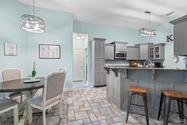 kitchen with decorative light fixtures, kitchen peninsula, a breakfast bar area, and gray cabinetry