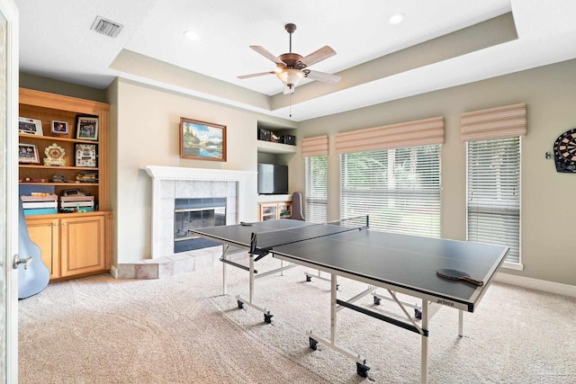 playroom with ceiling fan, light colored carpet, a tray ceiling, and a tiled fireplace