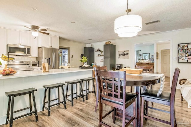 dining area featuring a textured ceiling, light hardwood / wood-style floors, ceiling fan, and crown molding