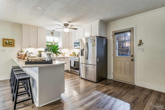 kitchen featuring dark wood-type flooring, stainless steel appliances, kitchen peninsula, a kitchen bar, and white cabinets